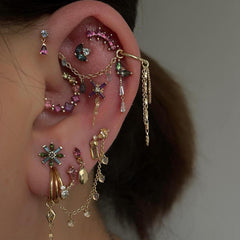 Close-up of an ear with multiple gold and gemstone earrings against a neutral background
